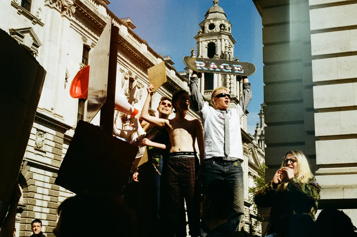 a group of people holding signs and placards. one of them holding a scateboard which says RAGE.