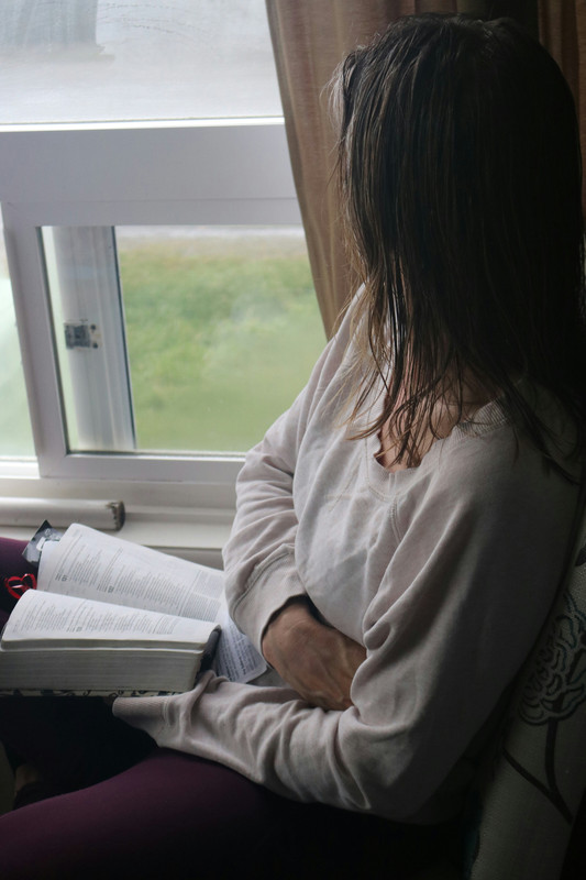 Woman reading a book by window, phone set aside