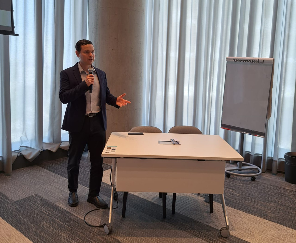 Luis Rafaschieri apresentando com entusiasmo em uma sessão profissional, utilizando microfone e quadro branco.