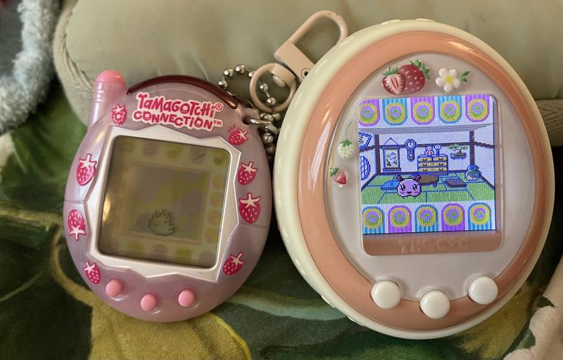close up photograph of a tamagotchi plus color device and a tamagotchi connection device. a sakuramotchi is visible on one screen and ALIBI is on the other