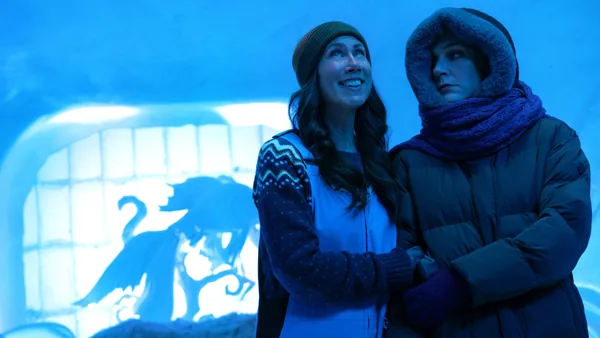 still frame from pluribus showing Carol and Helen on vacation in an ice hotel several years before the events of episode 1. Both are dressed warmly. Carol looks kind of grumpy and withdrawn but Helen looks elated to be there.