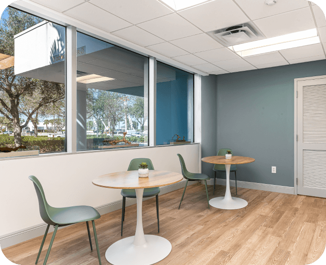 Modern coworking space with a long counter adorned with green plants. The area features well-lit ceilings and ample seating arrangements along the counter.