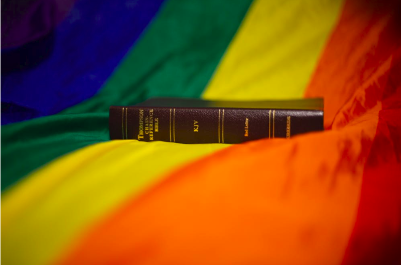 A photo of the Bible sitting on top of the LGTBQ+ rainbow flag.