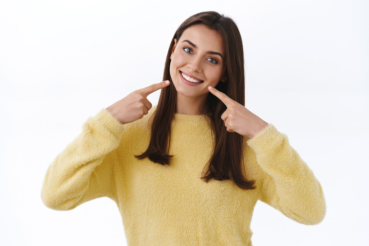 feminine young attractive brunette woman promote dental services pointing perfect white smile mouth