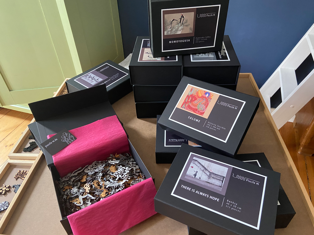 Stacks of ClairDeBois puzzle boxes, open box with pink tissue and wooden puzzle pieces
