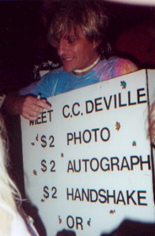 C.C.DEVILLE Wears A Sandwich Board With Prices For Meet & Greet