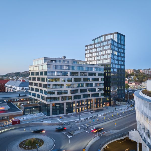 MIMO-huset i Mölndal – en modern, glasad kontorsbyggnad där bland annat AI Business School håller till, fotograferad i kvällsljus med omgivande stadsmiljö och trafik som rör sig runt byggnaden.