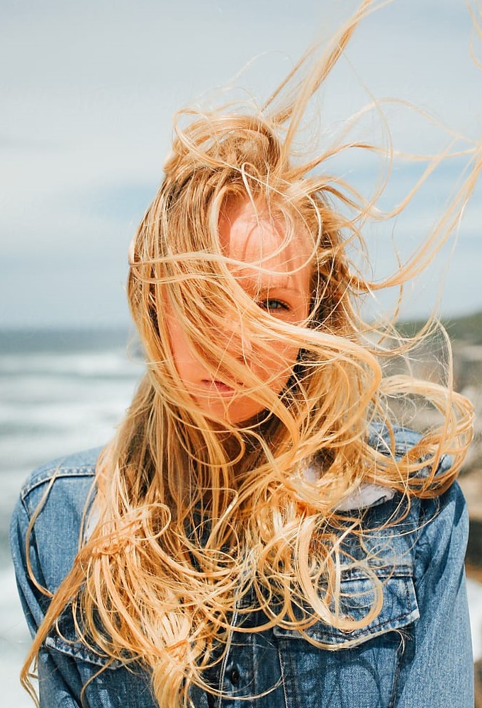 A girl in a denim jacket with blond hair in the wind by the sea