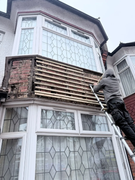 Exterior renovation before - worker on ladder removing old cladding from bay window