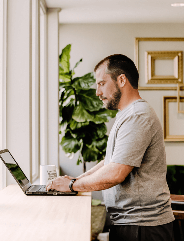 Man standing and working on a laptop at a counter in a coworking space, side view.