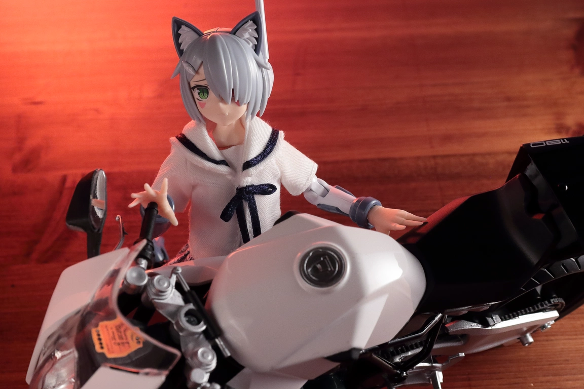 A top view of a 1:12 scale diecast model of the RC8 in white and “Variable Fighter Girls” Kairos girl wearing a 1/12 White Collar Check Sailor Uniform Set in blue