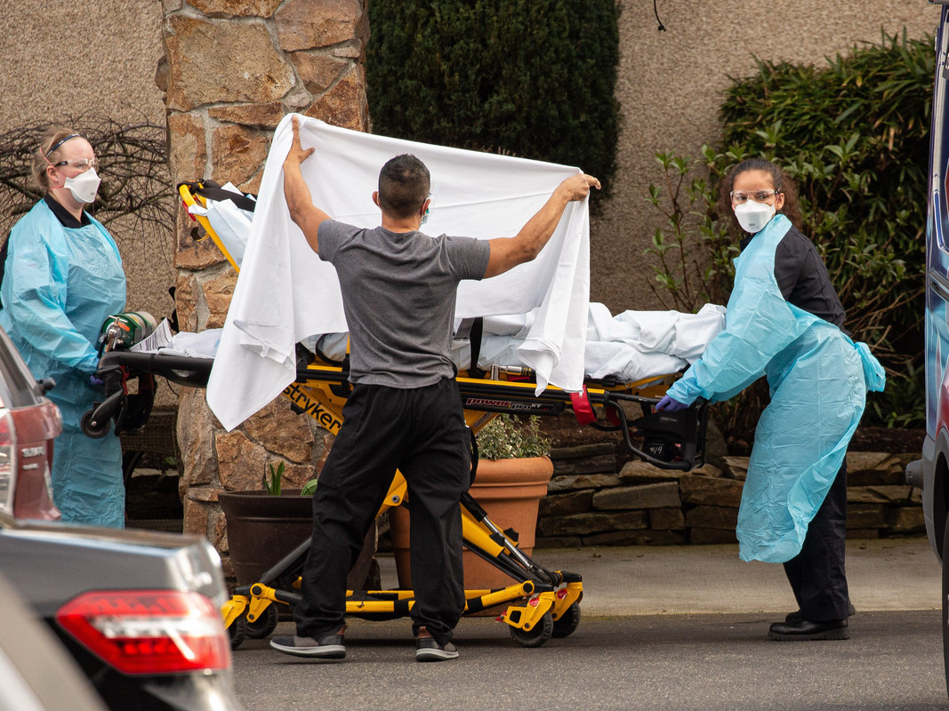 Healthcare workers transport a patient on a stretcher into an ambulance at Life Care Center of Kirkland, Washington