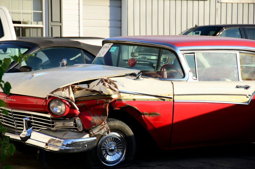 a vintage red and white car with severe front-end collision damage parked outdoors