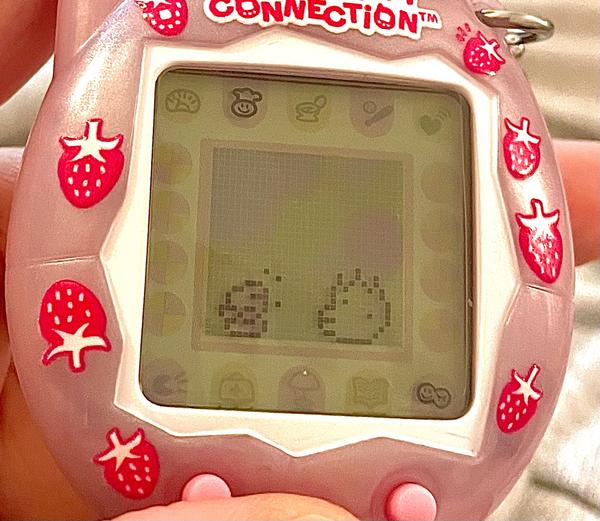 up close photo of a tamagotchi connection device (2024 rerelease) showing ALIBI happily eating a burger