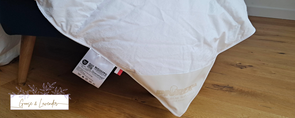 Zbliżenie na szczegóły kołdry puchowej Piorex White Flower, kant z labelem i szyciem