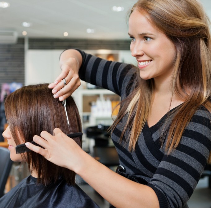 A hairstylist cuts a bob haircut for a blonde girl
