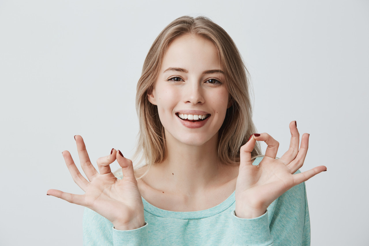 i m doing great glad happy young blonde female blue sweater smiling broadly making ok gesture with b