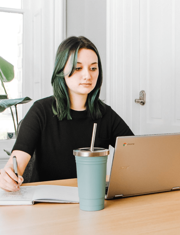 Woman sitting at a desk with a laptop, looking thoughtfully aside in a bright office.