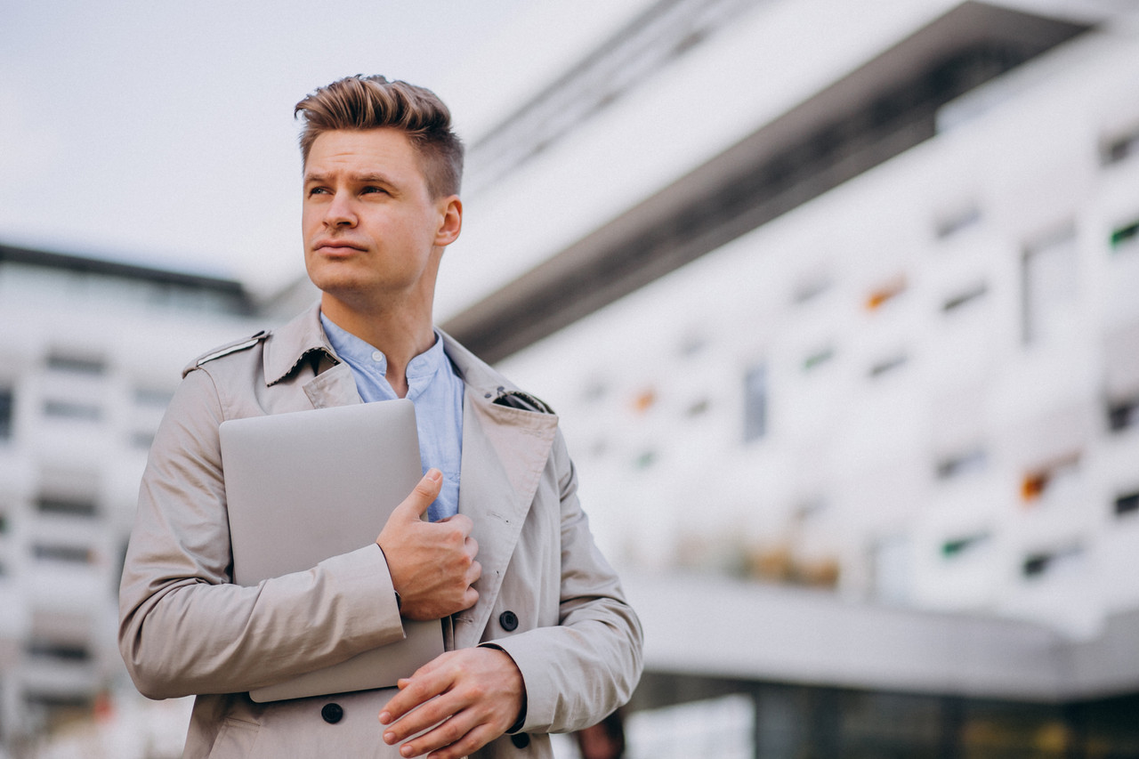 young business man standing with laptop outside business centre