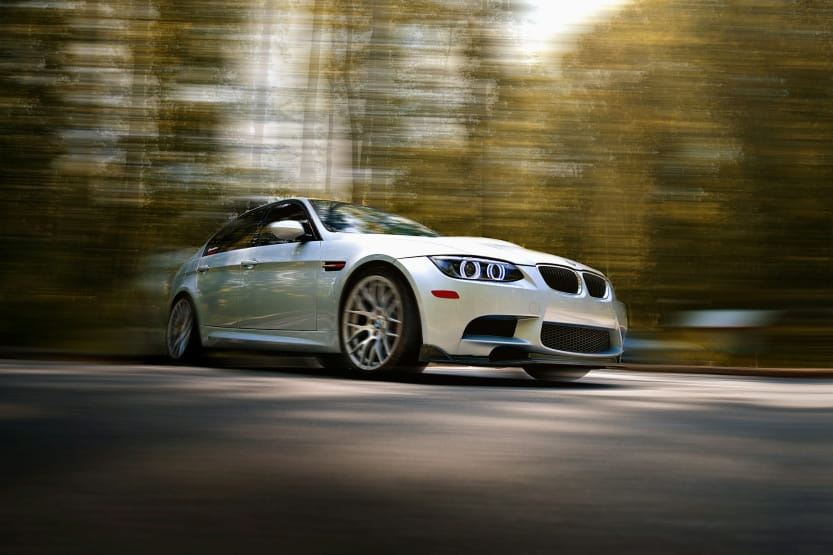 a white BMW sports car driving quickly on a forest road