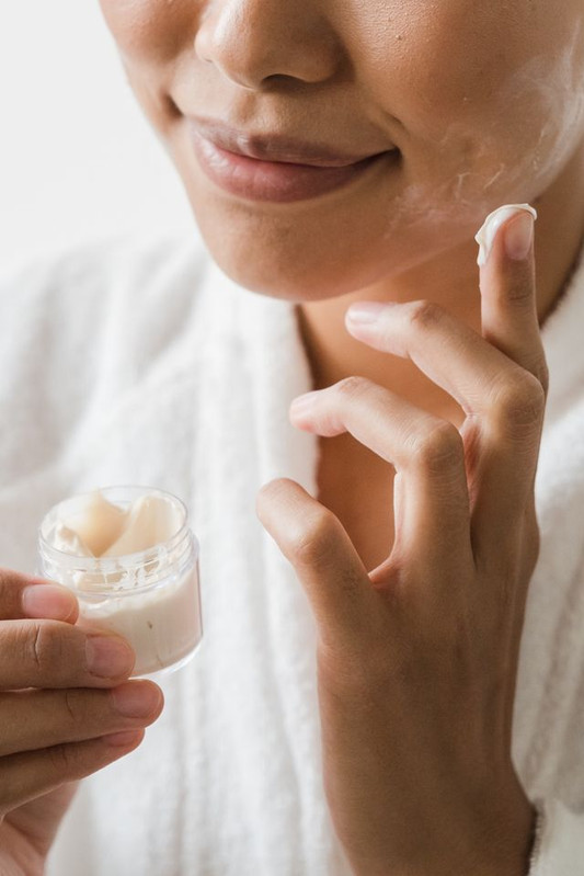  a woman applying moisturizer to keep her skin protected and well-hydrated in fall. 