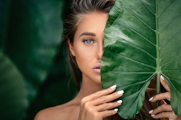 luxe-portret-van-een-mooie-jonge-vrouw-met-natuurlijke-make-up-heeft-een-groot-groen-blad-op-wazig-g.jpg