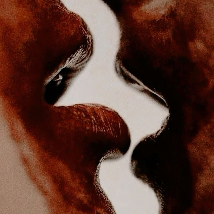 Um close-up de dois pares de lábios se aproximando para um beijo, em tons de vermelho e marrom escuros.