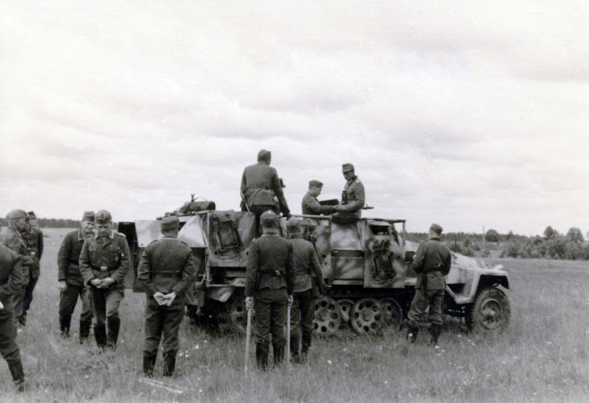 Mehrere Wehrmachtssoldaten stehen bei einem Militärfahrzeug.