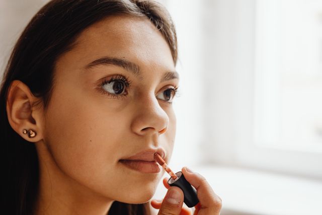 a woman applying nude lipstick 