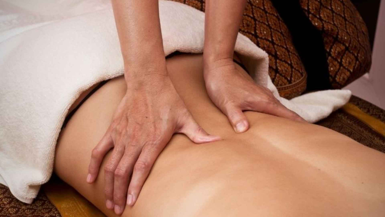 Kỹ thuật viên dùng hai tay ấn giãn cơ dọc cột sống thắt lưng để giảm đau lưng dưới khi ngồi lâu
