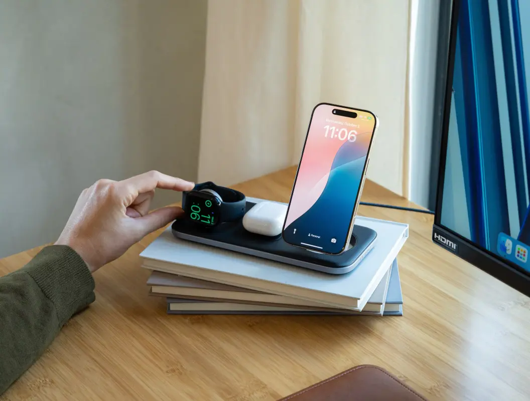 Base de carga Satechi Qi2 Trio cargando un iPhone, Apple Watch y AirPods en una mesita de noche.
