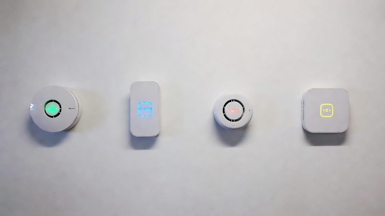 Four smart smoke detectors mounted on a white wall showing different designs and LED indicators