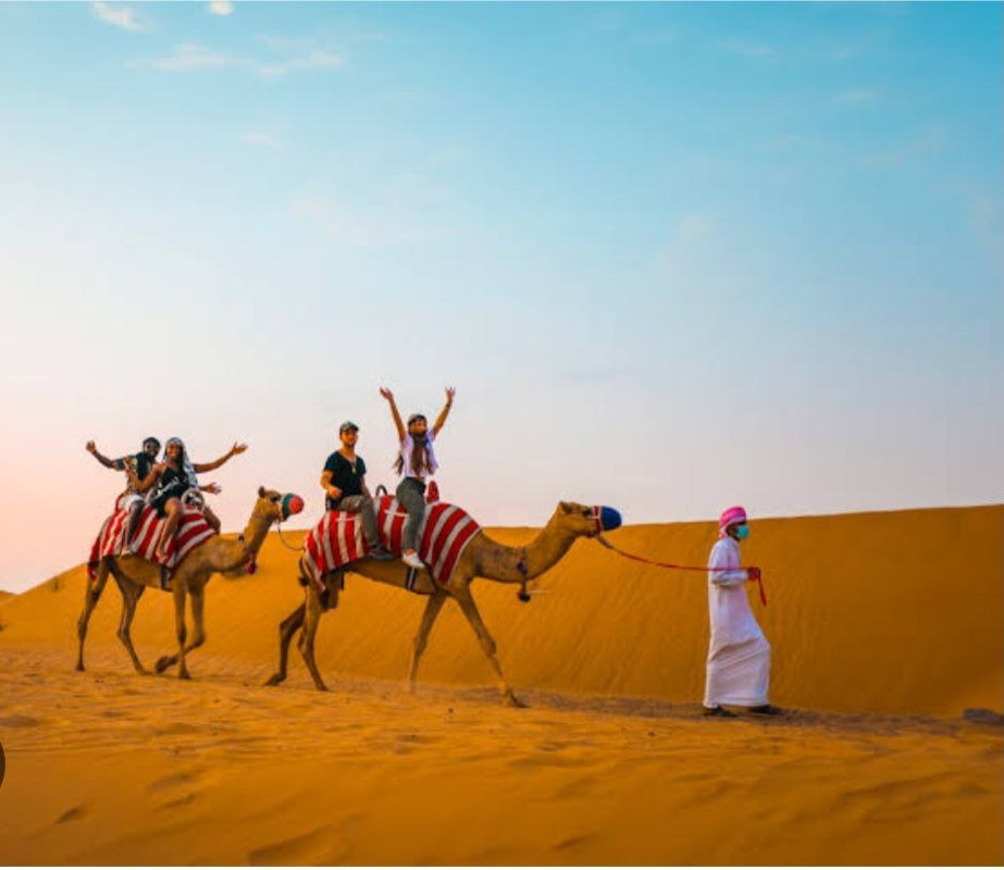 Arab man leading camels in the Dubai desert with happy tourists riding on them