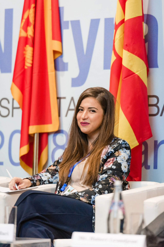 Arlinda at a conference, seated in front of flags.