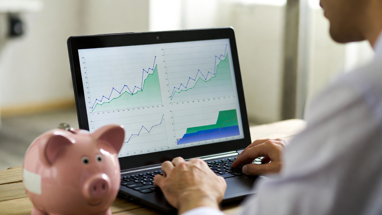 A person looking at a laptop screen showing growth charts, with a piggy bank in the foreground