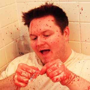 Man ripping a bandaid while covered in fake blood