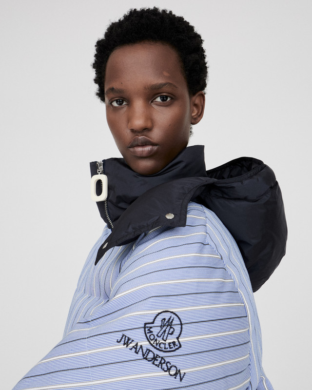 Moncler x JW Anderson FW25 – Piumino femminile a righe blu e bianche Modella indossa il piumino a righe blu e bianche Moncler x JW Anderson FW25 con logo ricamato