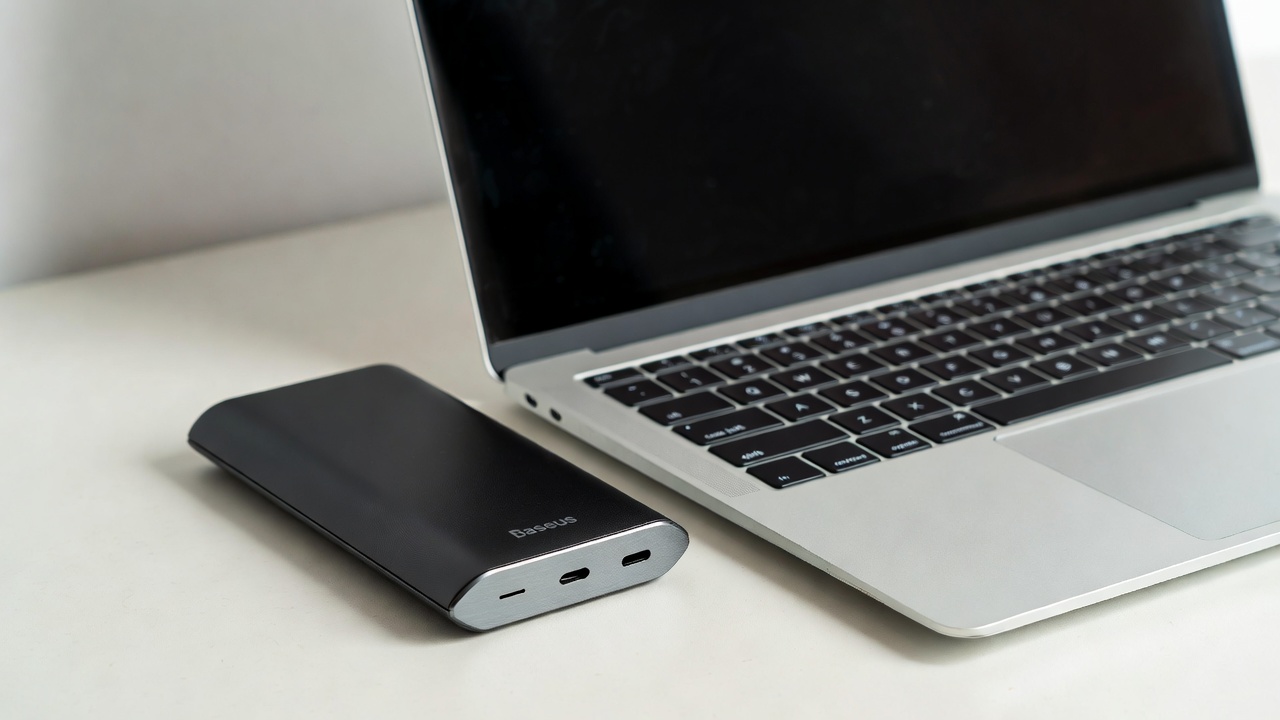 Baseus Blade 100W ultra-slim power bank next to a laptop showing slim profile design