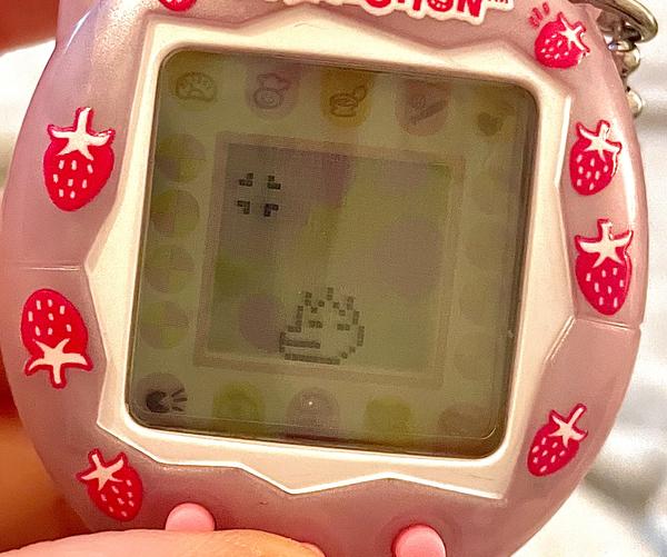 up close photo of a tamagotchi connection device (2024 rerelease) showing alibi as a teenager and she is grimacing in annoyance
