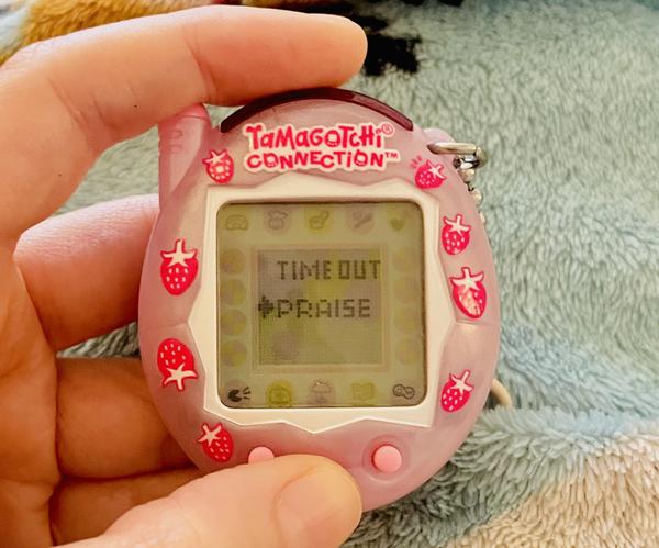 up close photo of a tamagotchi connection device (2024 rerelease) showing two options: time out or praise. I am selecting praise