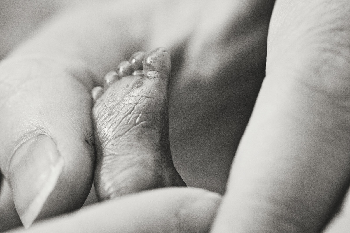 Black and white image of a tiny baby foot - which measures only as big as the top joint of a fingertip- is shown surrounded by an adult hand.