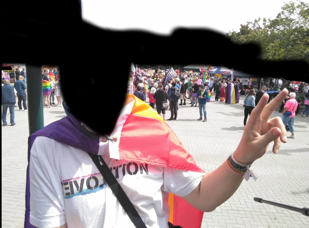 an edited selfie of cuntsuela wearing a white tee shirt with the word revolution printed on it in a font that looks like shitty spray paint with part of the word revolution reversed to spell love being highlighted by a pedophile flag they also have a pedo flag bracelet made of a shitty fabric hair tie and are wearing a rainbow flag as a cape