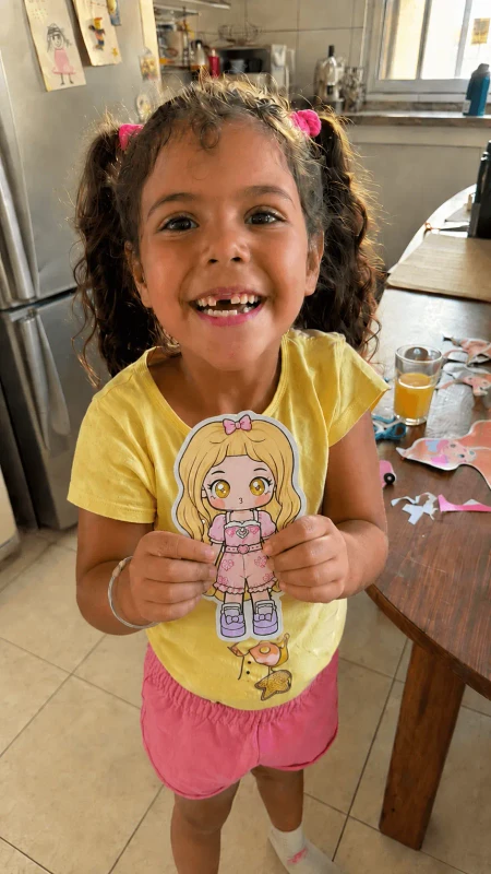 Alice sorrindo mostrando uma boneca de papel que acabou de montar