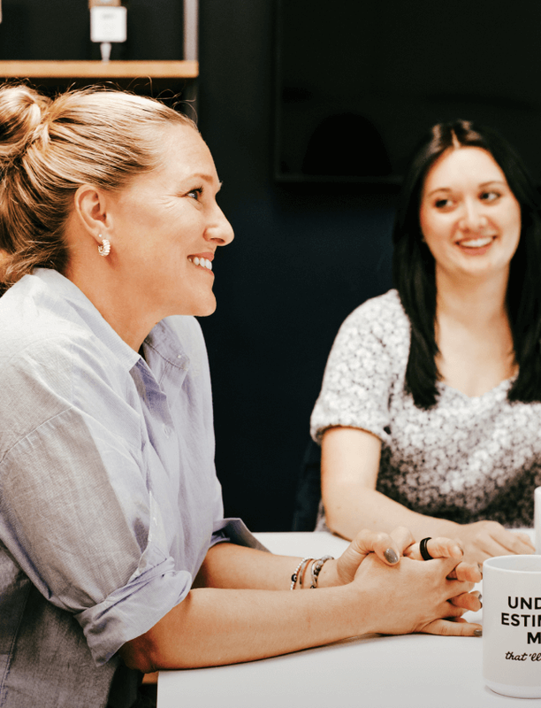 Two women smiling and conversing across a table in a shared workspace.