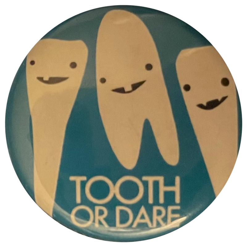 a blue pin with three teeth on it [each of which having only one or two teeth] and that says 'tooth or dare'