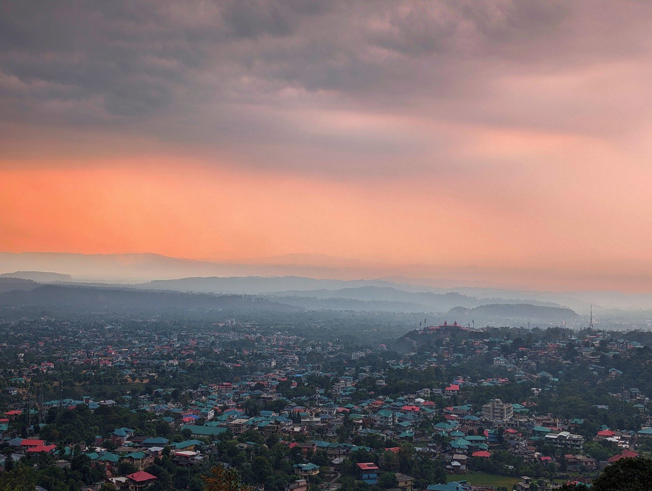 Dharamshala's buildings and stadium spread across the hillside with the Dhauladhar range rising behind