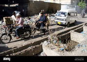 commuters pass through near an open sewerage drain and huge heap of CM5N7X