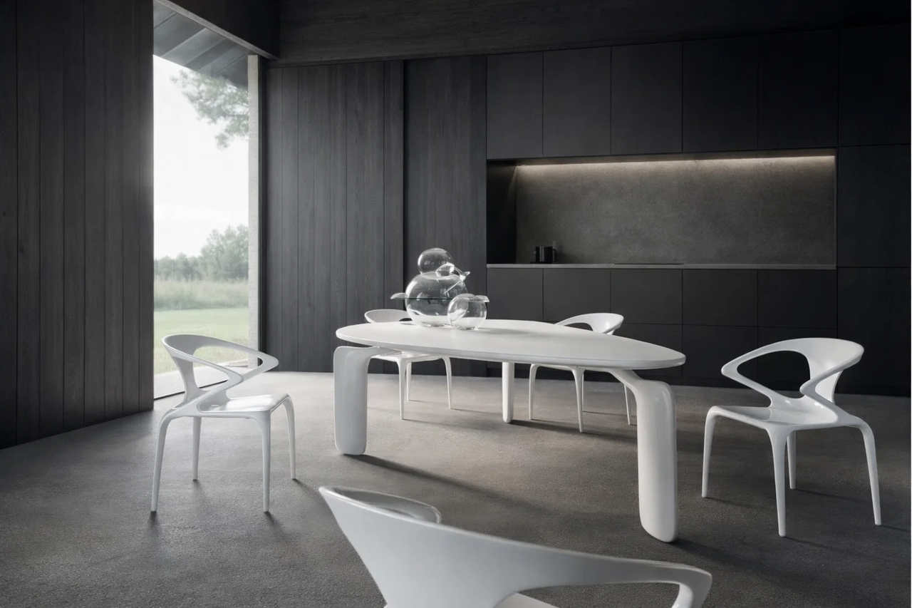 Minimalist dining room with white sculptural table in a dark setting.