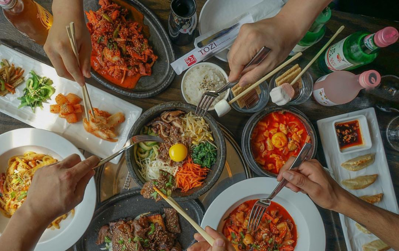 Overhead restaurant lifestyle food photography with shared Korean dishes and hands dining together