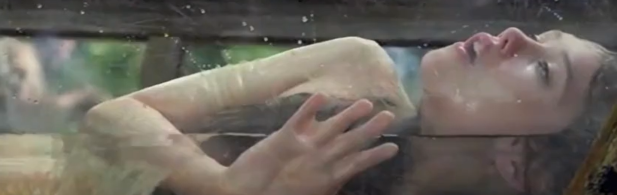 A sexy nude girl lying in the water with her breasts exposed.